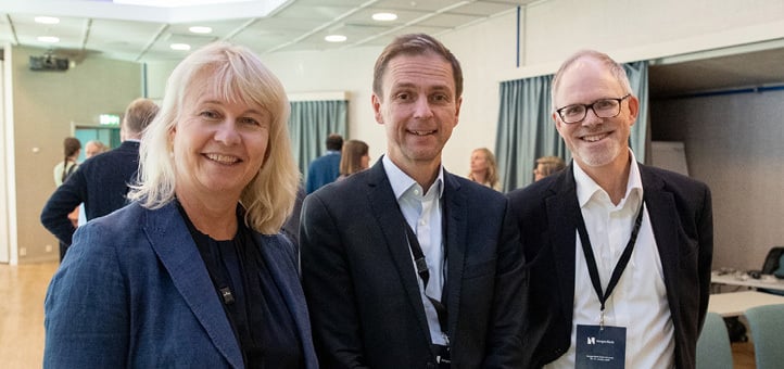 A woman and two men standing with accreditation cards around their necks looking at the camera