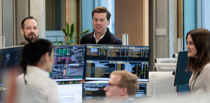 Three male and two female employees sitting and monitoring market information on computer screens