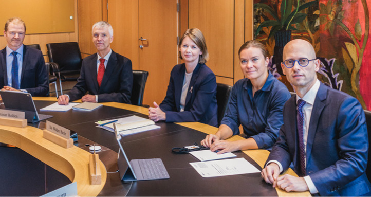 A group of two women and three men sitting at a circular boardroom table looking at the camera