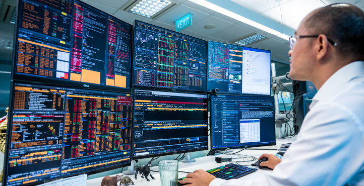 A male employee sitting in front of many screens with market information