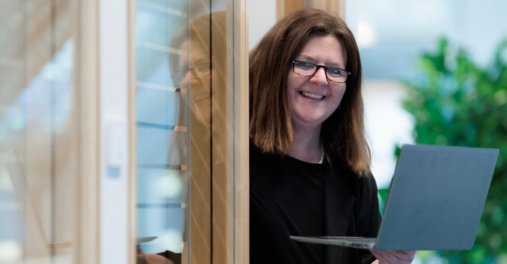 A female employee coming out of a room holding an open laptop in her hand