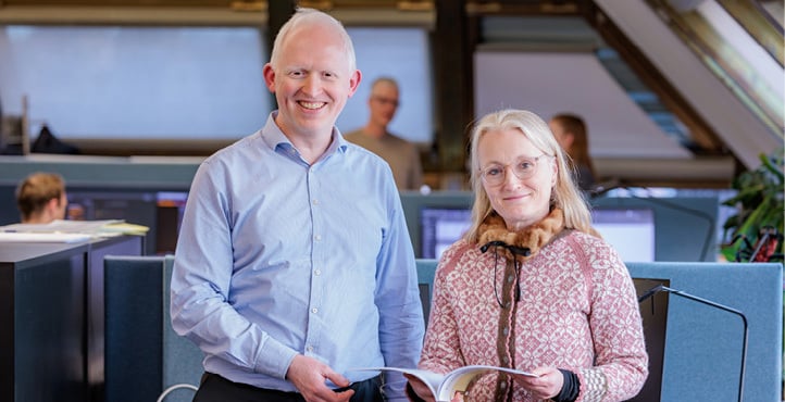 A male and a female employee standing and holding a report in their hands