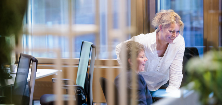 Two female employees in an open office looking at a computer screen