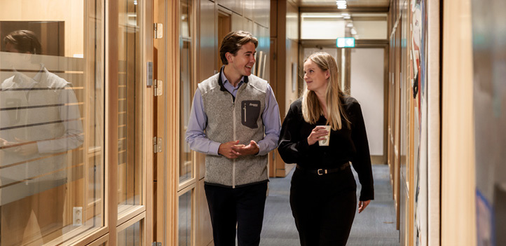 A male and female employee walk down a corridor talking to each other