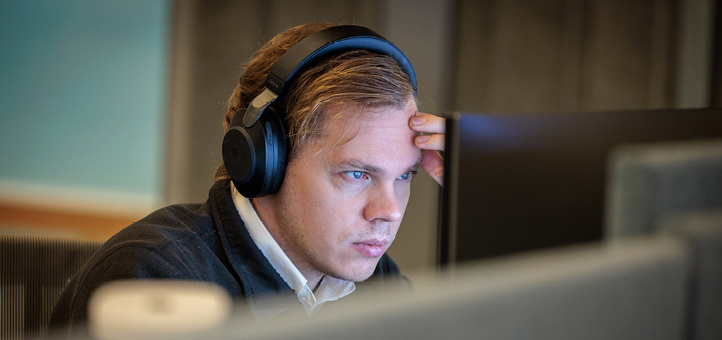 A male employee with headphones sitting and looking at a computer screen