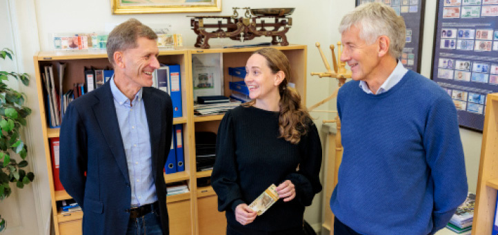 Two men and a woman standing and talking, the woman is holding a NOK 500 banknote