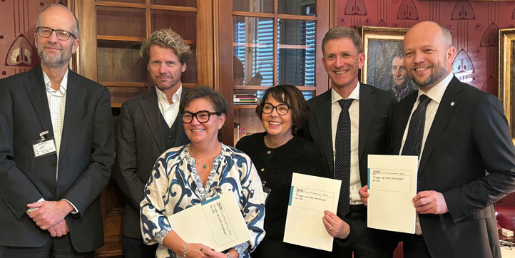 A group of two women and four men standing and holding up reports