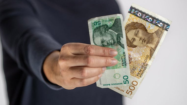 En hånd holder to sedler - en 50-lapp med portrett av Peter Christian Asbjørnsen og en 500-lapp med portrett av Camilla Collett
