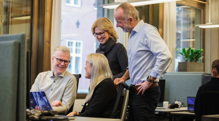 Two people sitting at a desk and two people standing behind them. 